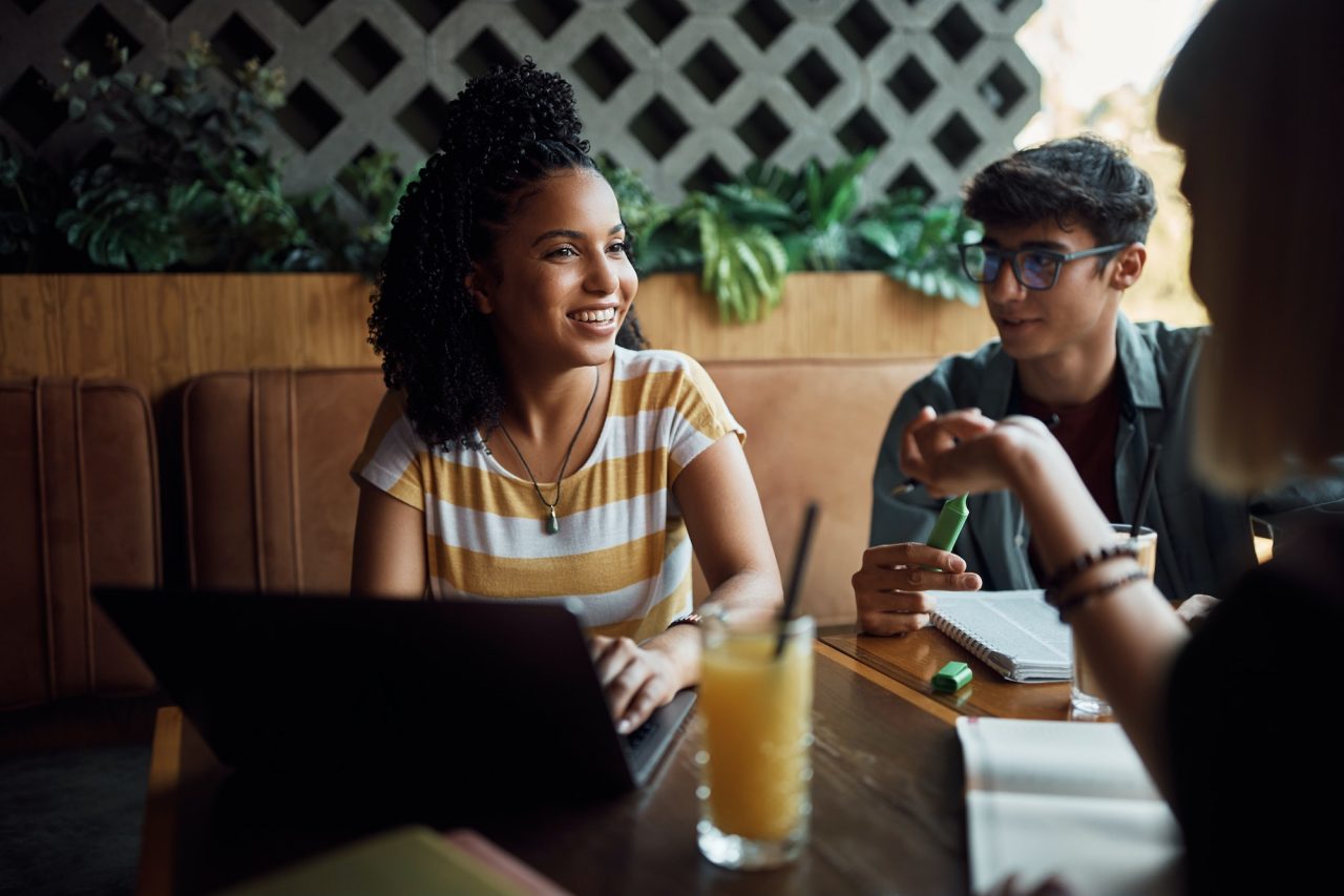 Happy Black Student Using Laptop While Learning With Her Friends In A Cafe