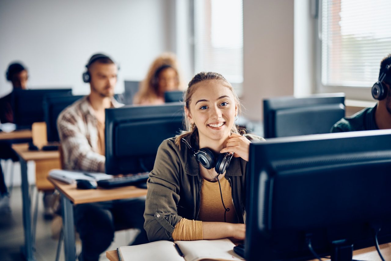 Happy Female Student Using Desktop Pc During Computer Class And Looking At Camera